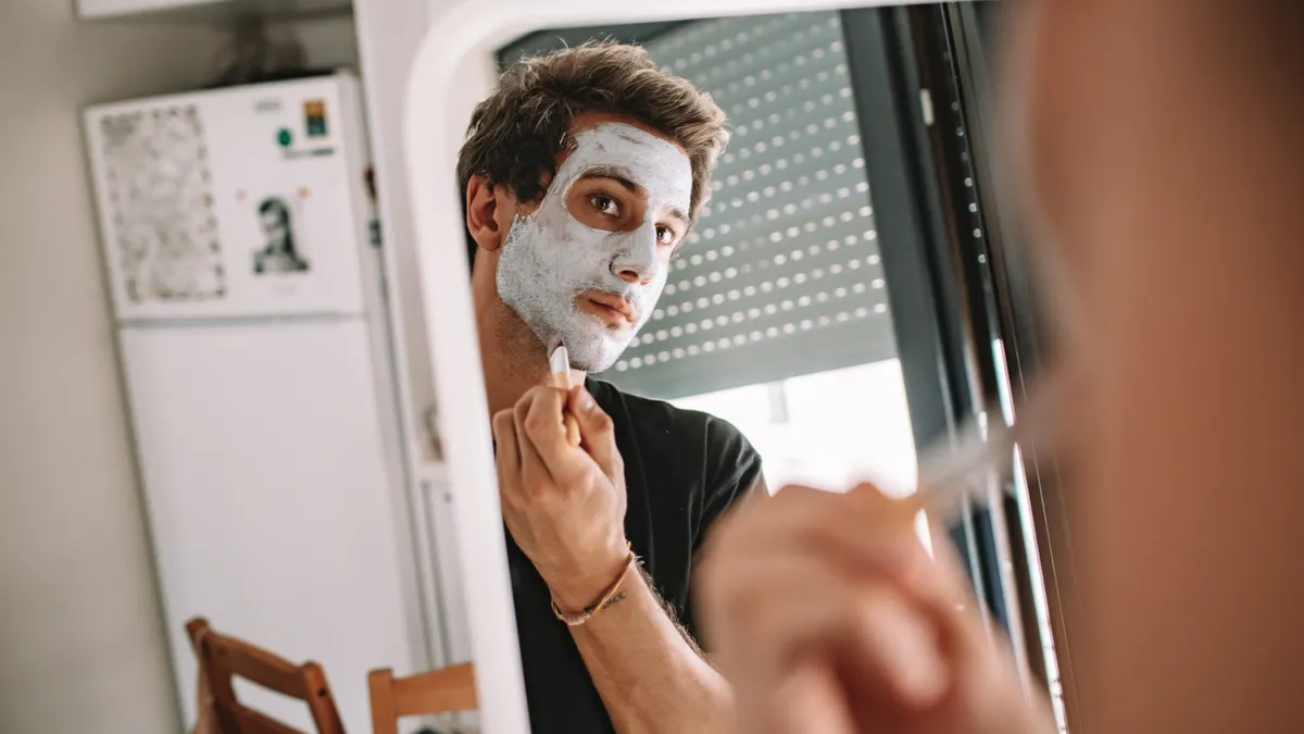 Man applying white face mask in mirror