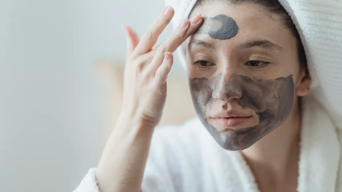 Woman applying dark facial mask to her face