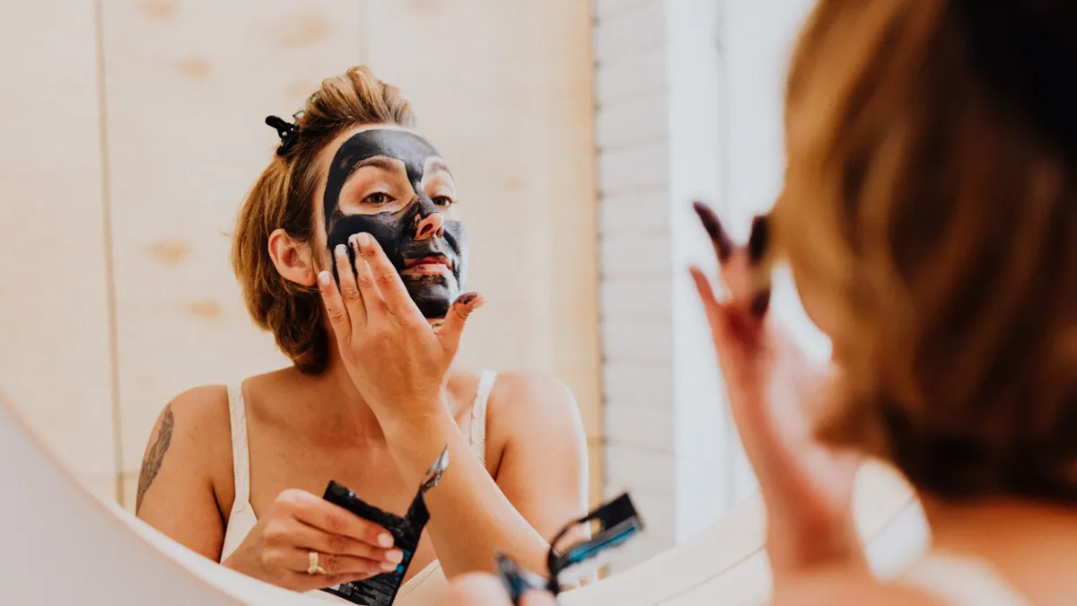 Woman applying black acne face mask in mirror